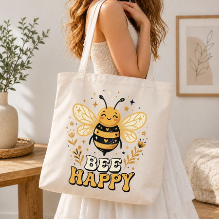 Person holding a tote bag with a bee design and 'Bee Happy' text in a home setting.