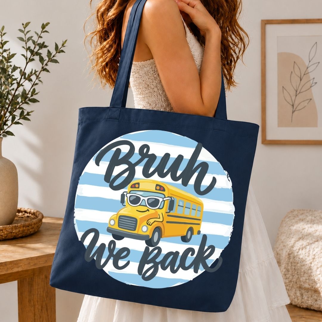 Navy tote bag with a yellow school bus graphic and 'Bruh We Back' text held by a person in a home setting.