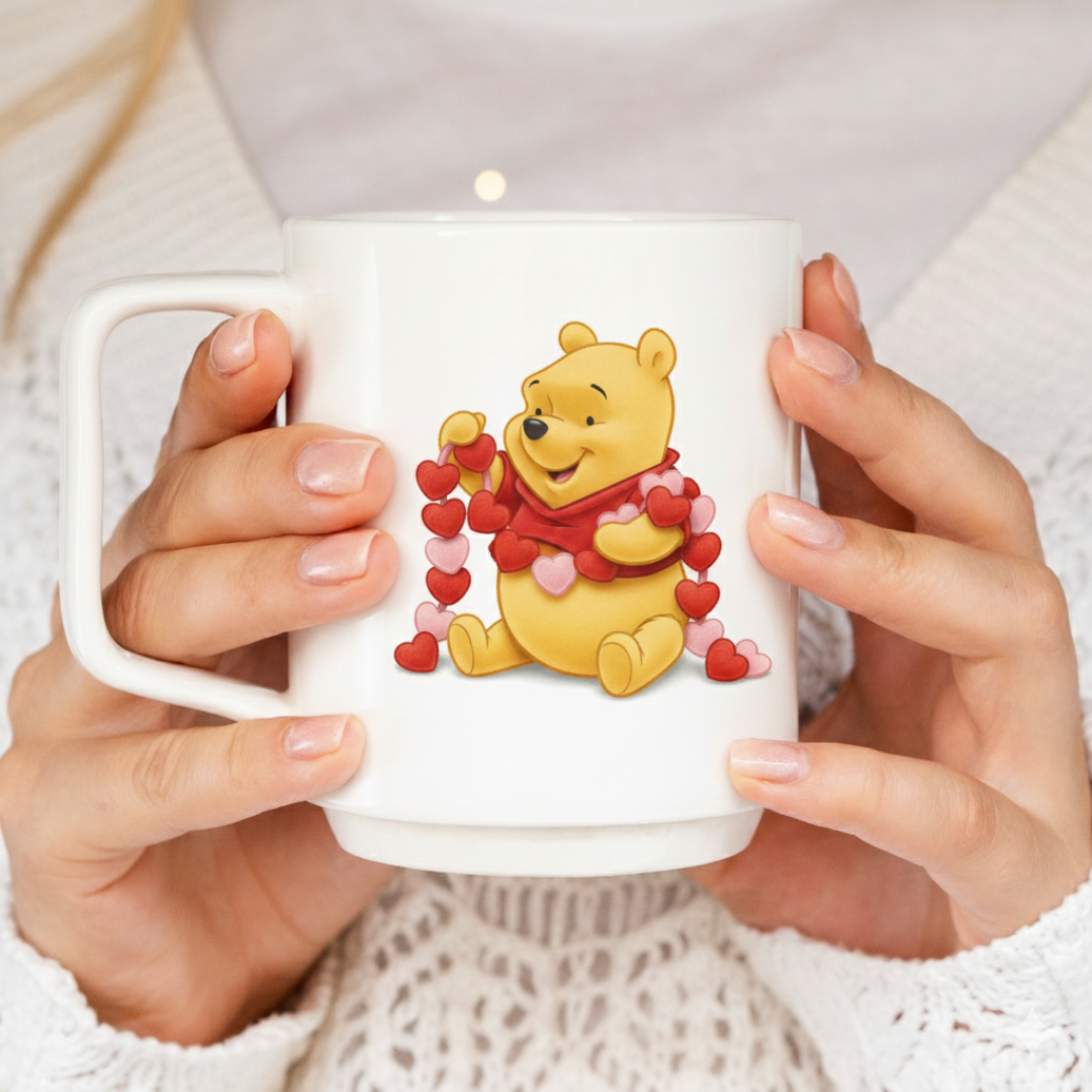 White mug with a cartoon bear design holding hearts, held by hands against a neutral background