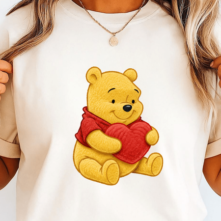 White t-shirt with a cartoon bear holding a heart design on a plain background