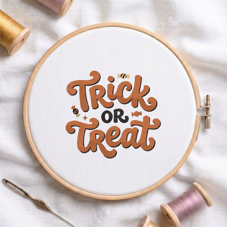"Trick or Treat" retro lettering with cute Halloween candies machine embroidery design shown in a wooden embroidery hoop on white fabric with thread spools and a needle