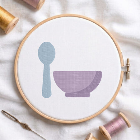 An embroidered blue spoon and purple bowl design stitched inside a wooden hoop on white fabric with sewing threads.