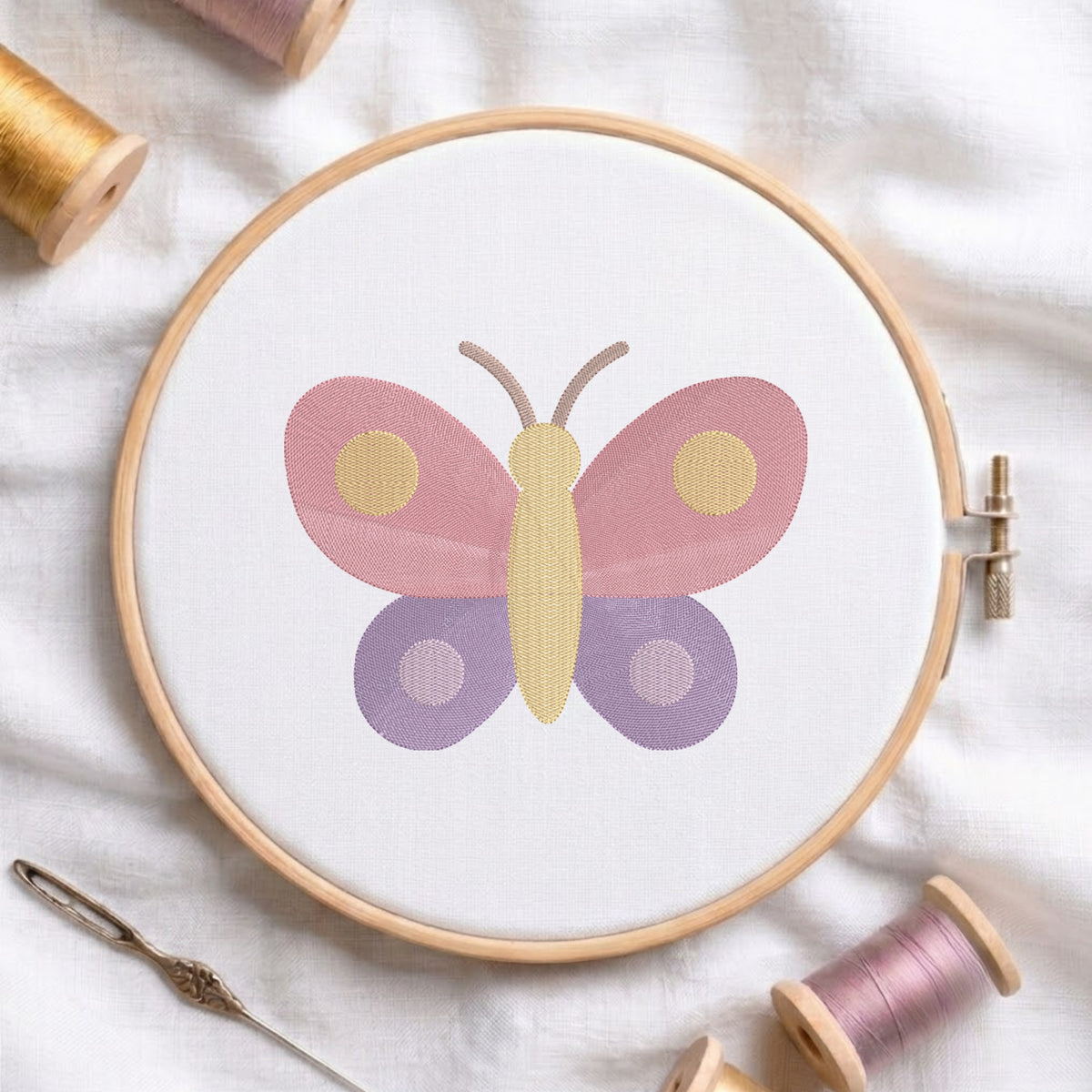 An embroidered colorful butterfly design with pink upper wings and purple lower wings stitched inside a wooden hoop on white fabric with sewing threads.