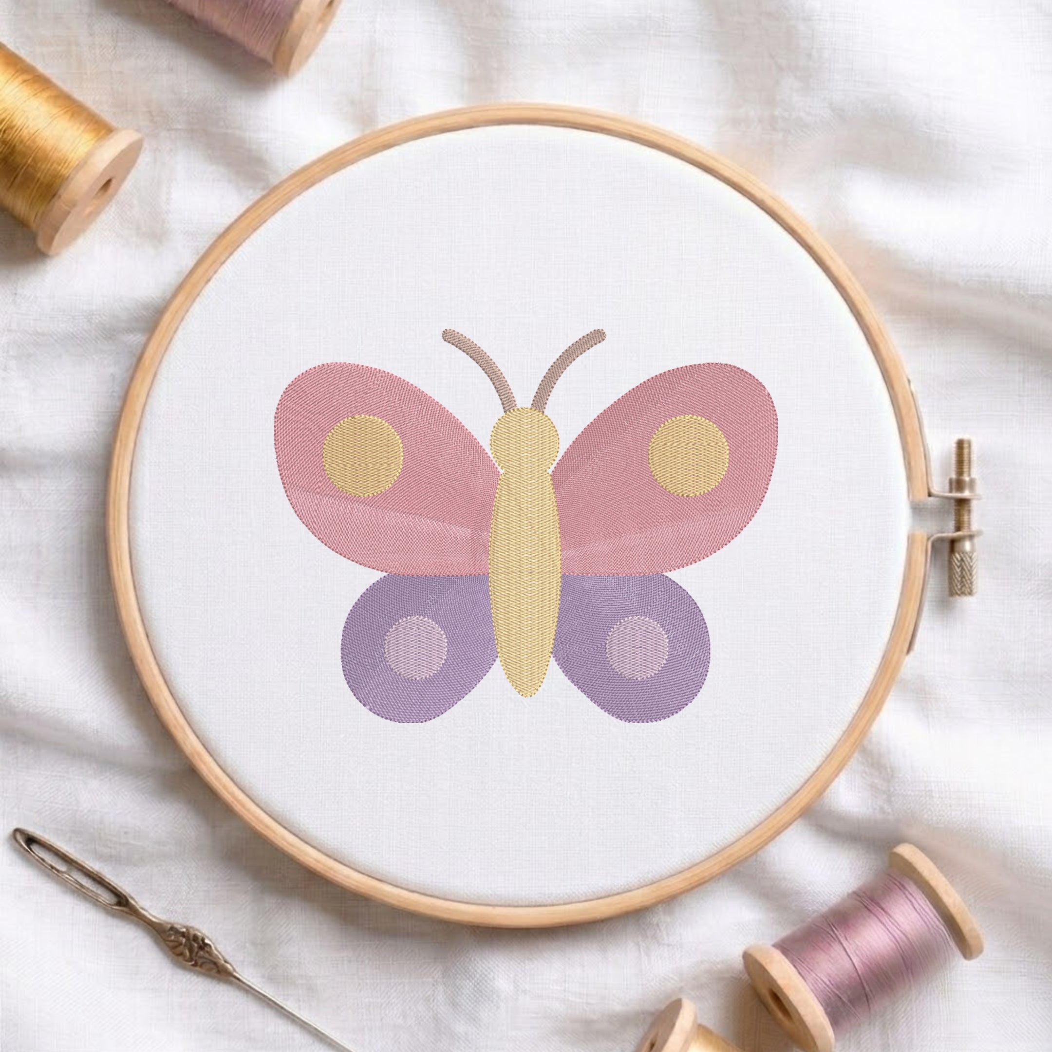 An embroidered colorful butterfly design with pink upper wings and purple lower wings stitched inside a wooden hoop on white fabric with sewing threads.