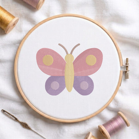 An embroidered colorful butterfly design with pink upper wings and purple lower wings stitched inside a wooden hoop on white fabric with sewing threads.