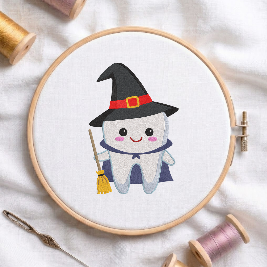 Cute witch tooth wearing a pointy hat and cape while holding a broom machine embroidery design shown in a wooden embroidery hoop on white fabric with thread spools and a needle