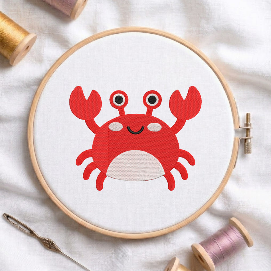 A round embroidery hoop holding white fabric with a red cartoon crab design, styled on white fabric with thread spools and a needle around it.