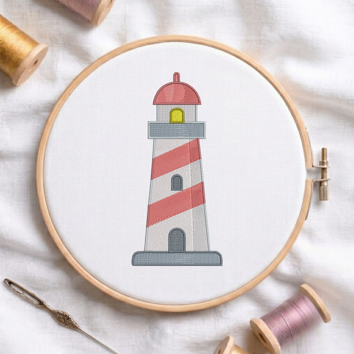 A circular embroidery hoop holding white fabric with a stitched lighthouse design. The lighthouse has red and white diagonal stripes, a gray base, a red dome, and a small yellow window.