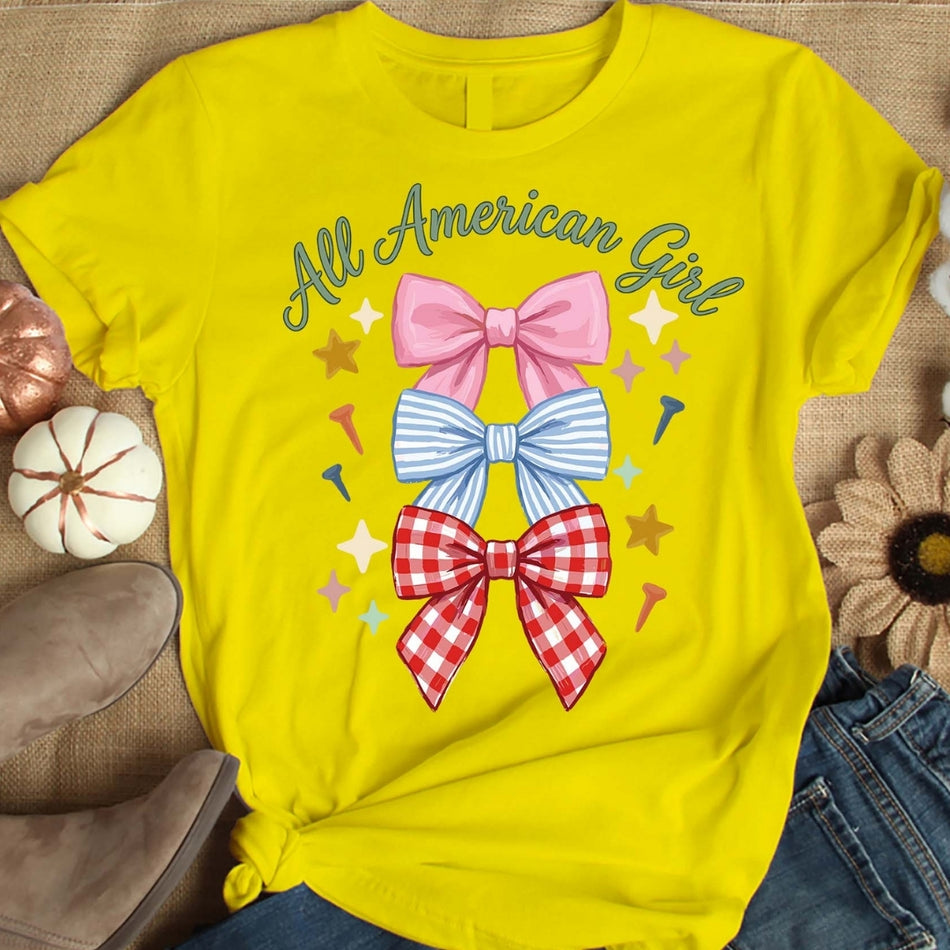 Yellow t-shirt with colorful bows and 'All American Girl' text on a textured surface.