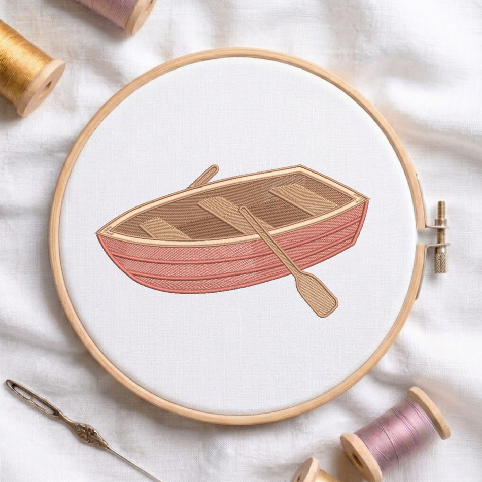 A circular embroidery hoop holds a white fabric with a stitched illustration of a pink and tan rowboat and oar. Spools of thread, a needle, and soft fabric are arranged around it in a styled flat-lay.