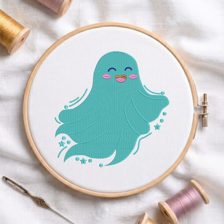 A wooden embroidery hoop holding white fabric with a cute teal octopus design stitched inside. The hoop is styled on a white fabric background with spools of thread and a needle nearby.