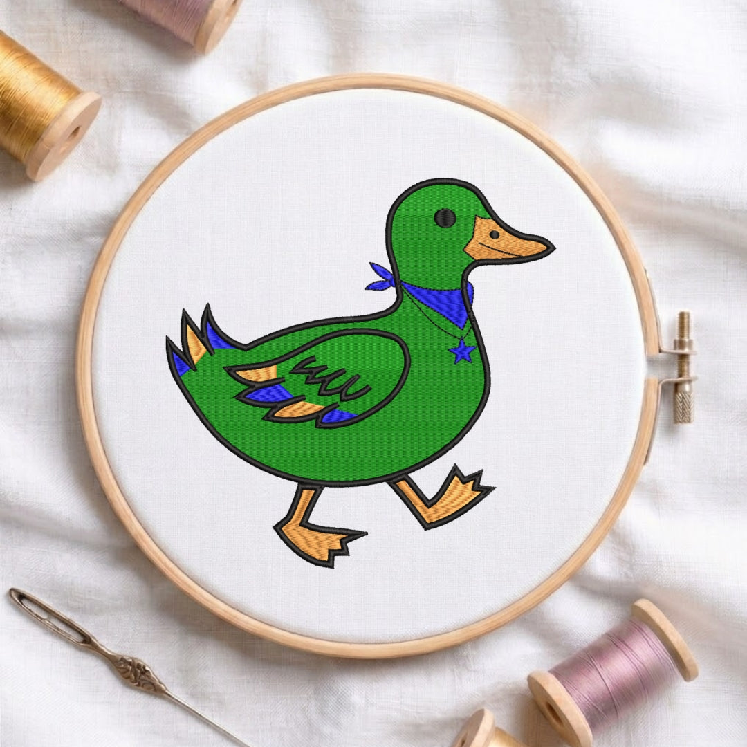 A circular embroidery hoop holding white fabric with a colorful stitched duck design. The duck is green with an orange beak and legs, a blue bandana, and small yellow accents.