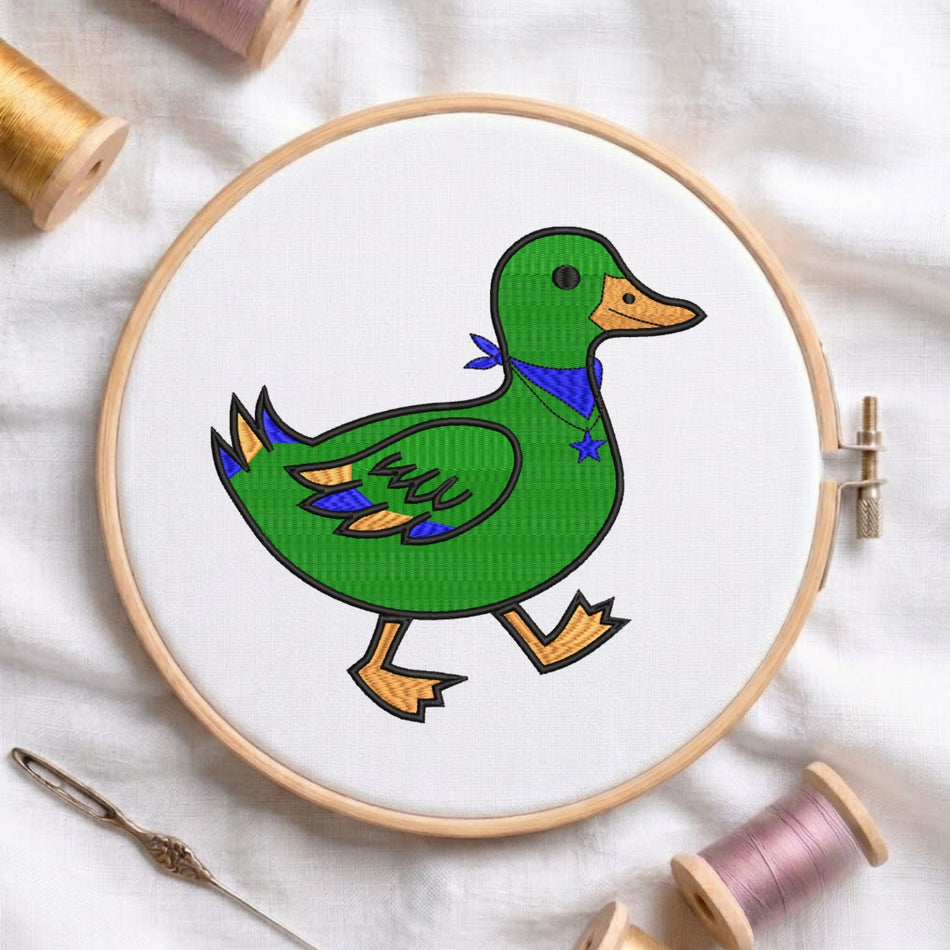 A circular embroidery hoop holding white fabric with a colorful stitched duck design. The duck is green with an orange beak and legs, a blue bandana, and small yellow accents.