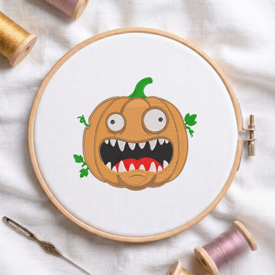 Funny spooky pumpkin with sharp teeth and wide eyes machine embroidery design displayed in a wooden hoop on white fabric with thread spools and a needle