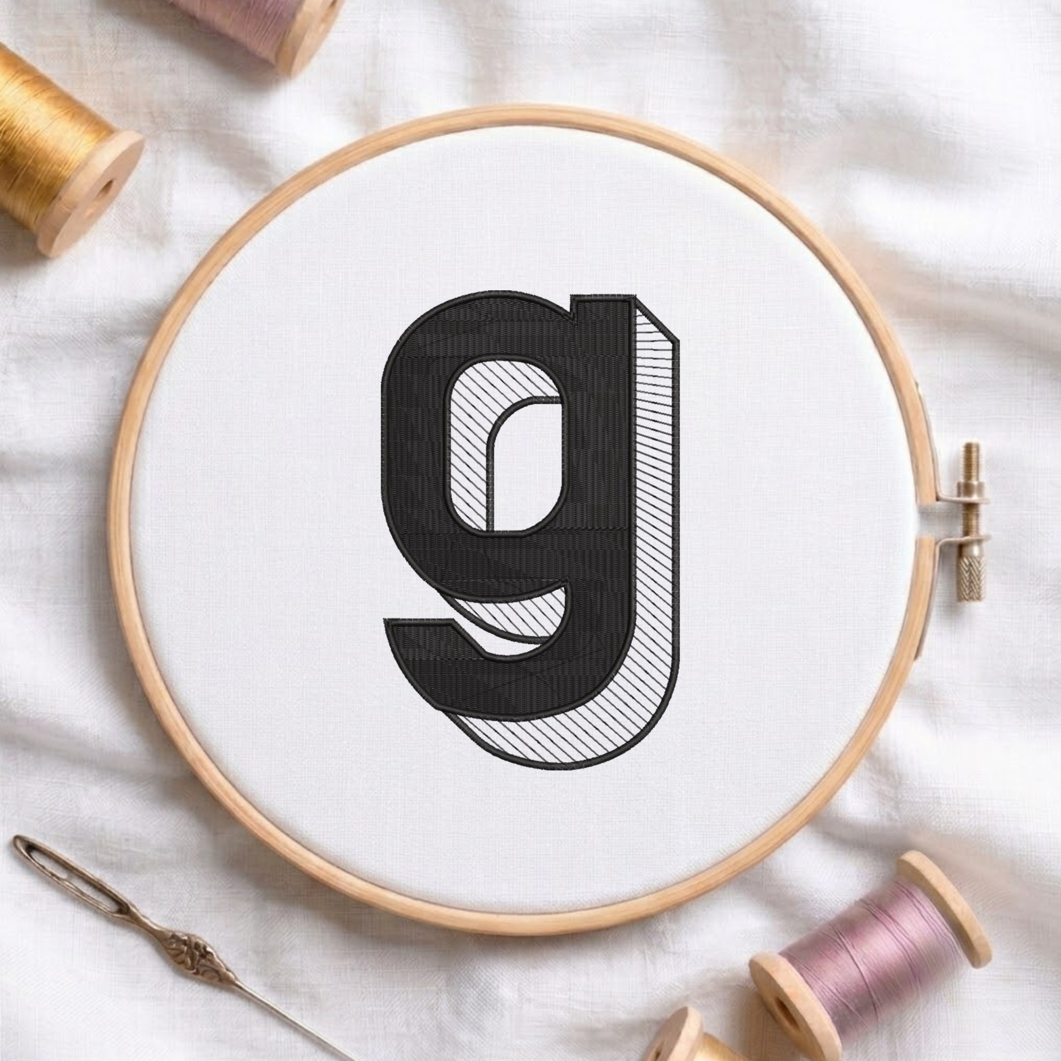 An embroidered 3D block lowercase letter "g" with striped shading texture, stitched inside a wooden hoop on white fabric with sewing threads.