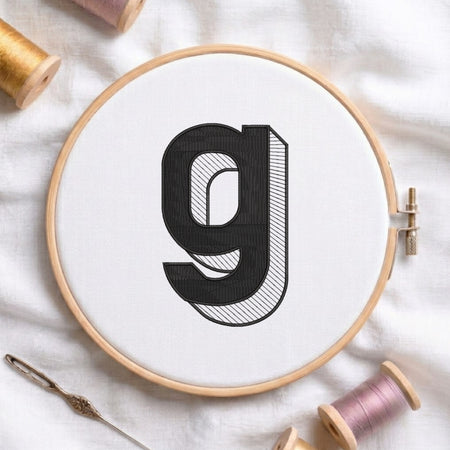 An embroidered 3D block lowercase letter "g" with striped shading texture, stitched inside a wooden hoop on white fabric with sewing threads.