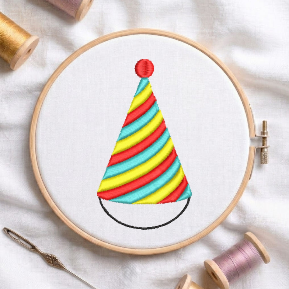 The party hat embroidery design secured in a wooden embroidery hoop, displayed with embroidery thread spools and a needle on a white fabric background.