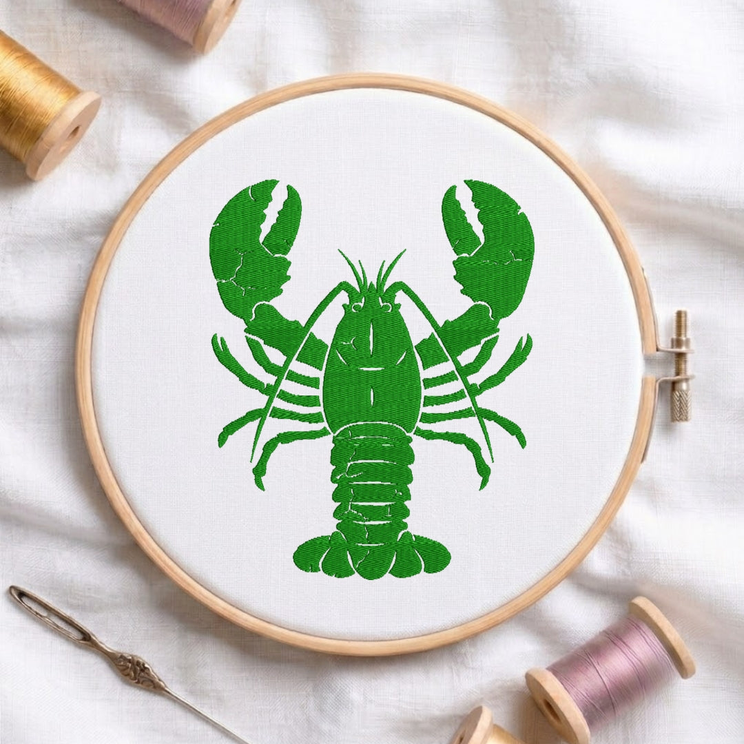A circular embroidery hoop holding white fabric with a bright green lobster design, styled on a white cloth with thread spools and a needle around it.