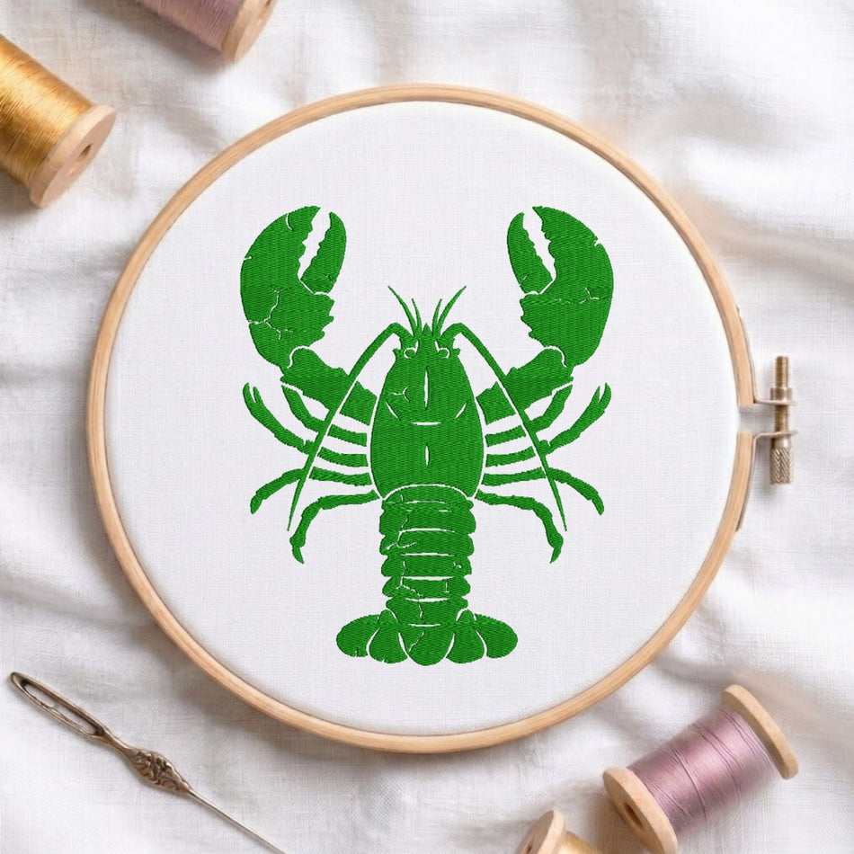 A circular embroidery hoop holding white fabric with a bright green lobster design, styled on a white cloth with thread spools and a needle around it.