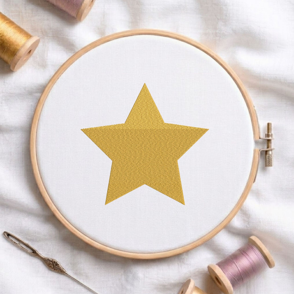 Golden star machine embroidery design displayed in a wooden hoop on white fabric with thread spools and a needle