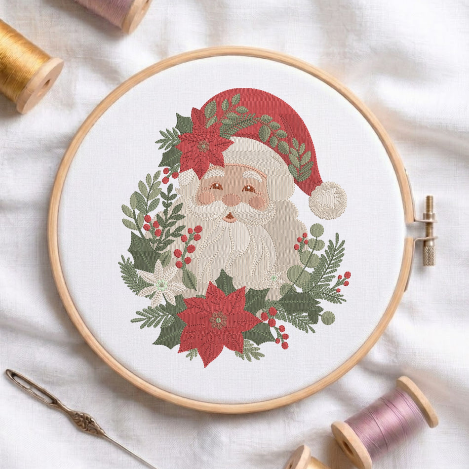 A circular embroidery hoop holds a festive Santa Claus design surrounded by poinsettias, holly leaves, and berries on white fabric. A needle lies at the lower left, and spools of thread are arranged around the hoop.