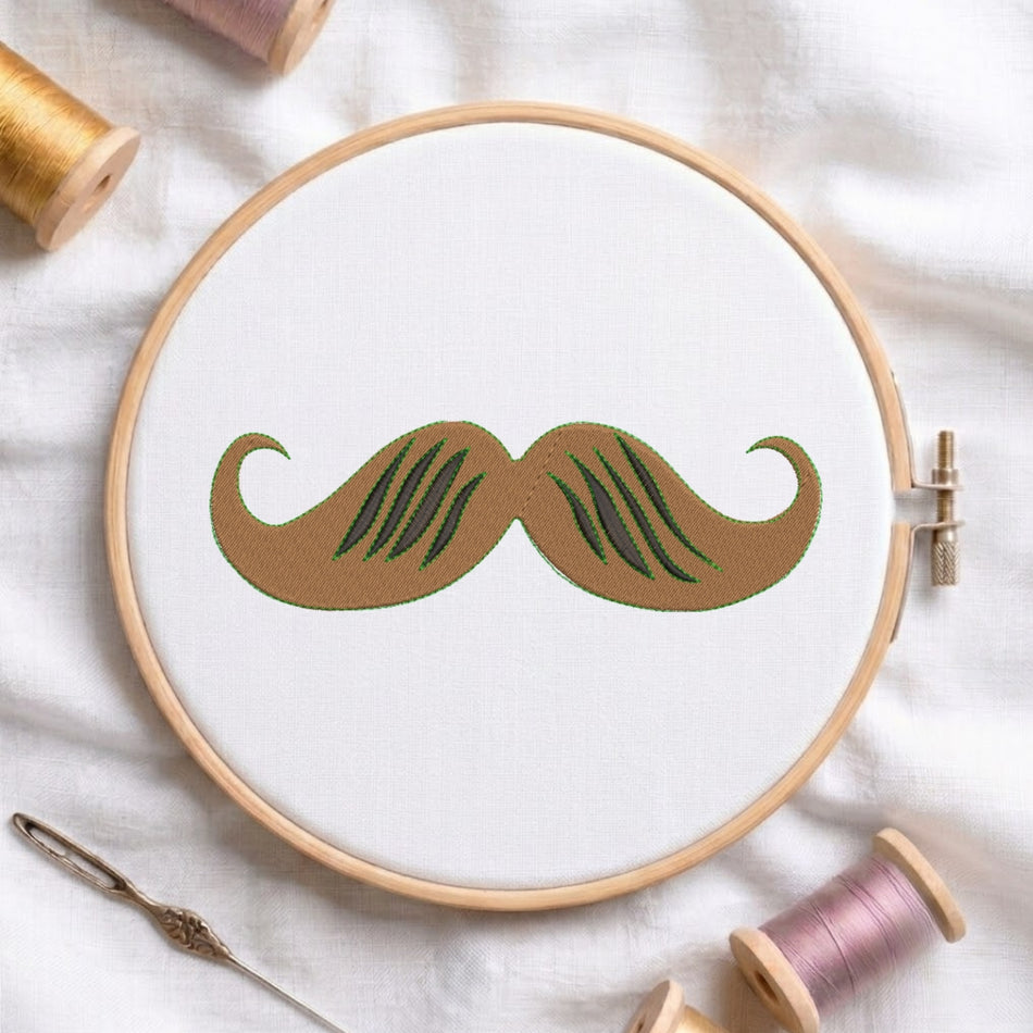 A wooden embroidery hoop holds white fabric with a stylized brown mustache design outlined in green. The hoop is styled on a white fabric background with spools of thread and a needle around it.
