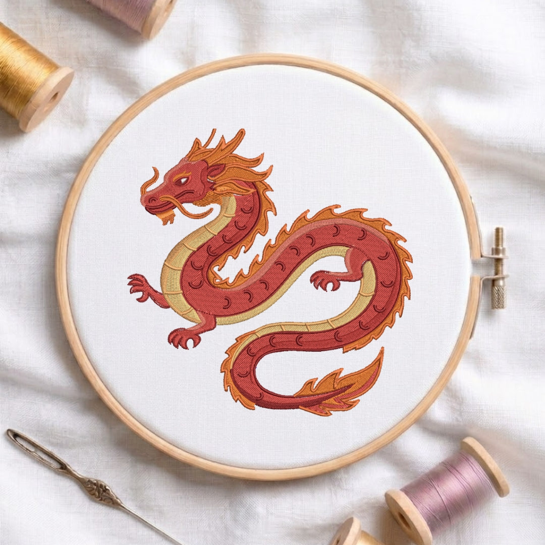 The dragon design is displayed inside a wooden embroidery hoop, surrounded by thread spools and a needle on a white fabric background.