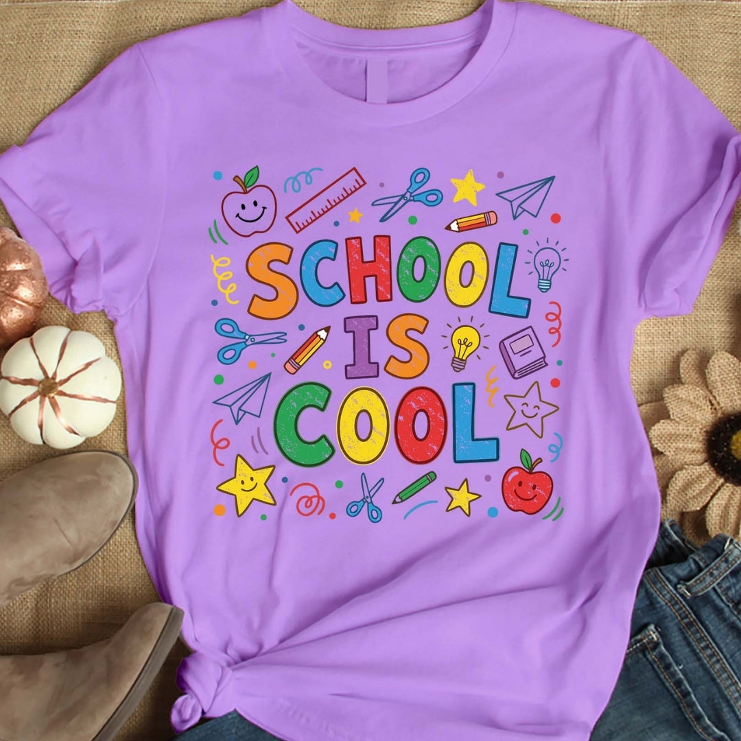 Purple t-shirt with colorful 'SCHOOL IS COOL' text and school-related graphics on a textured surface.