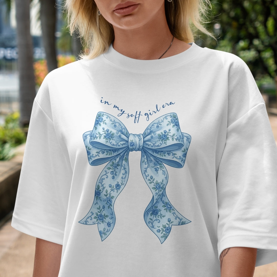 White t-shirt with blue floral bow design and text worn by a person outdoors.