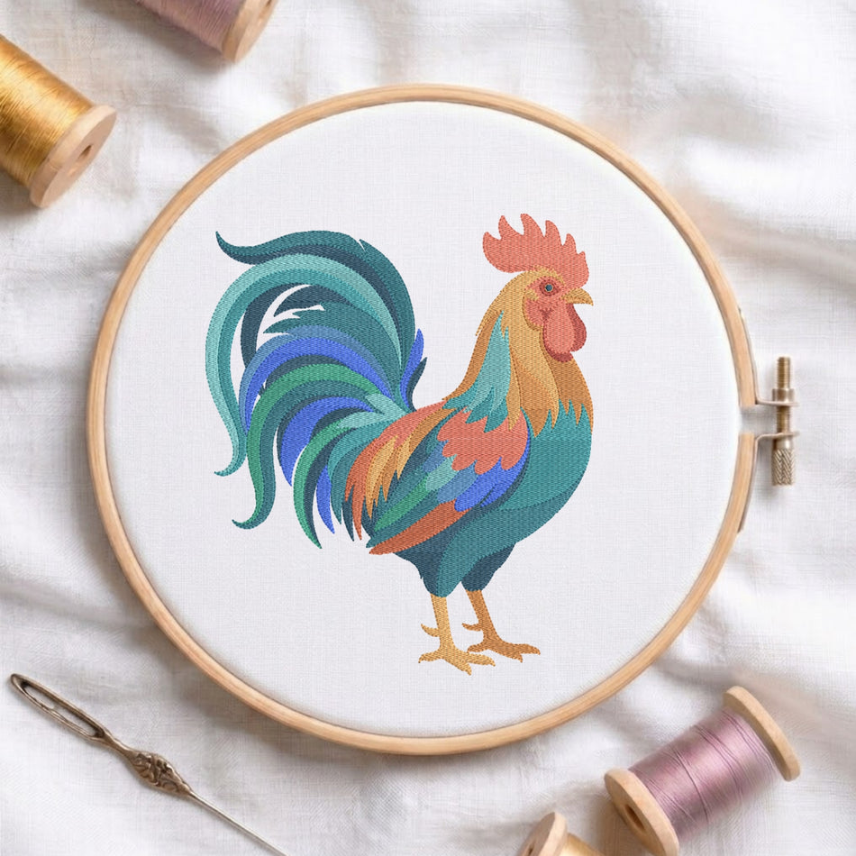 A white fabric stretched inside a wooden embroidery hoop featuring a detailed, colorful embroidered rooster design with blue and green tail feathers, alongside wooden thread spools.