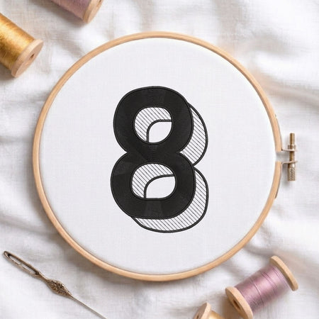 An embroidered 3D block number "8" with striped shading texture, stitched inside a wooden hoop on white fabric with sewing threads.