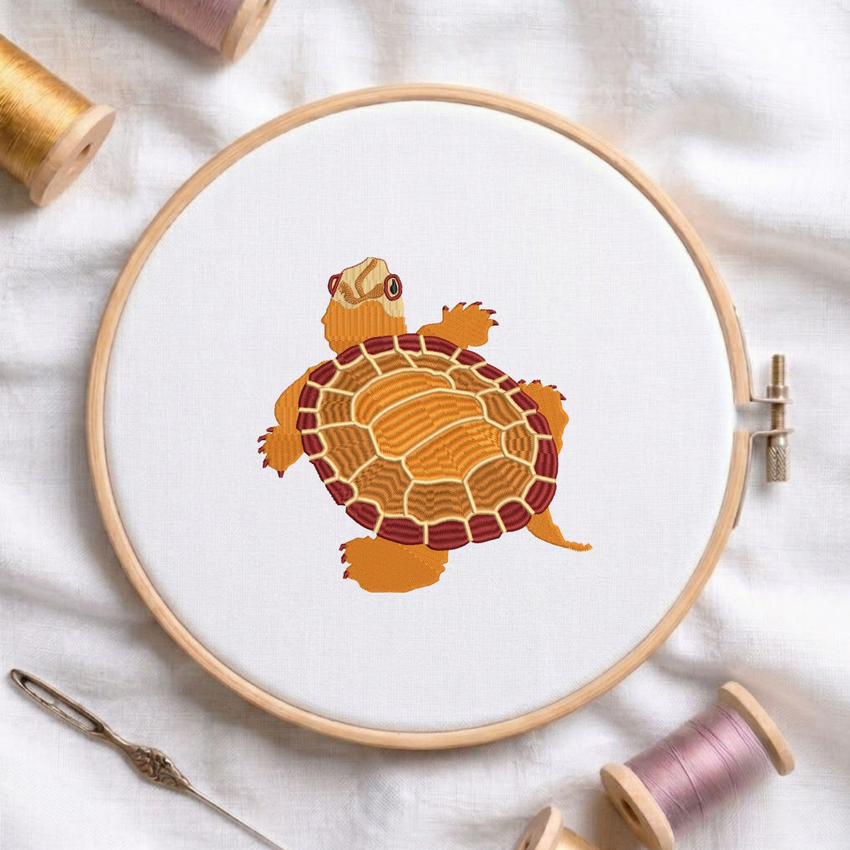  Turtle machine embroidery design displayed in a wooden hoop on white fabric with thread spools and a needle   