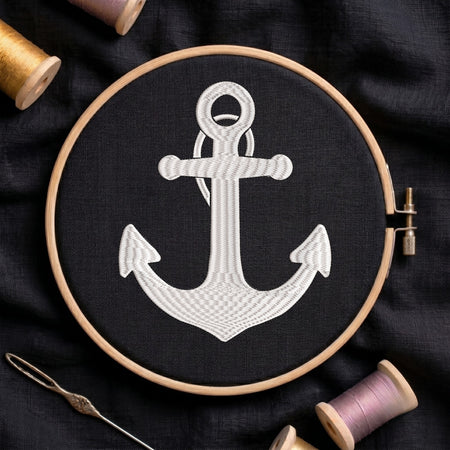 Embroidery hoop with a white anchor design on black fabric, surrounded by spools of thread.