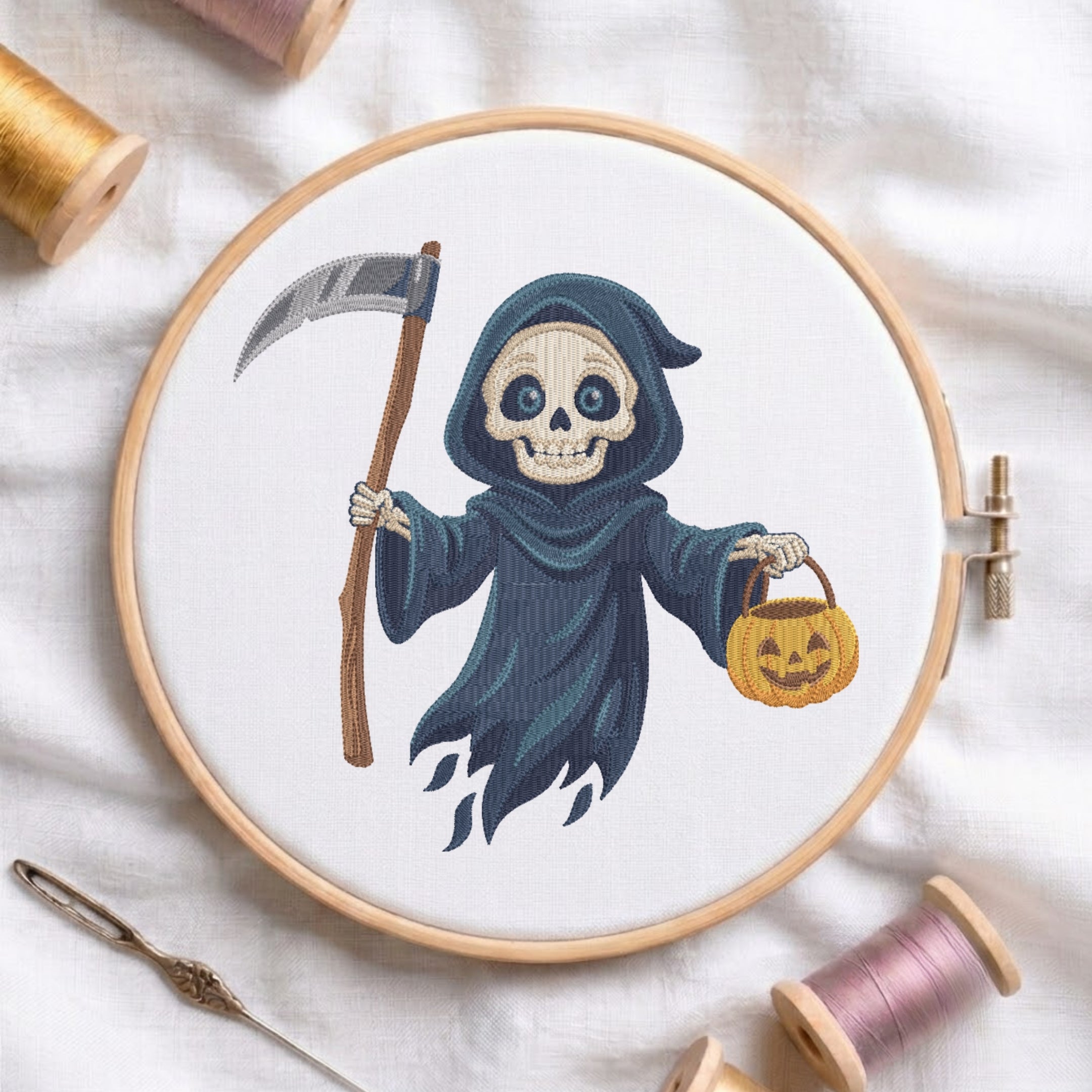 A circular embroidery hoop displays a stitched design of a skeleton in a dark blue hood holding a scythe and a jack-o'-lantern bucket. The hoop is styled on a white fabric background with spools of thread, a needle, and wooden embroidery hoops.