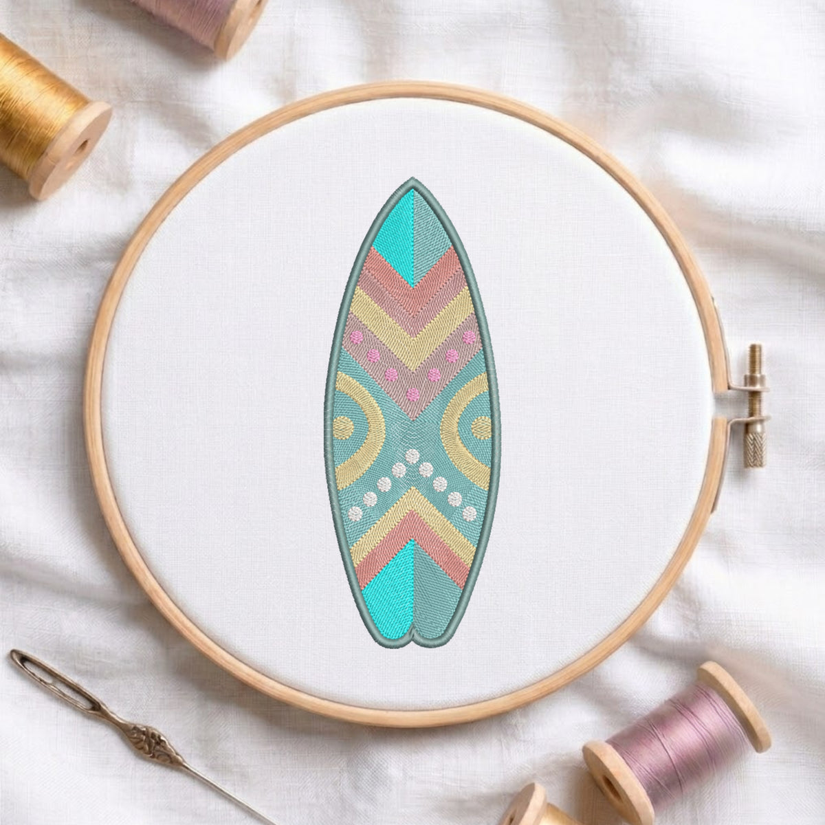 A wooden embroidery hoop holds a white fabric with a colorful surfboard design stitched in the center. The surfboard pattern features teal, pink, yellow, and beige geometric and circular motifs.