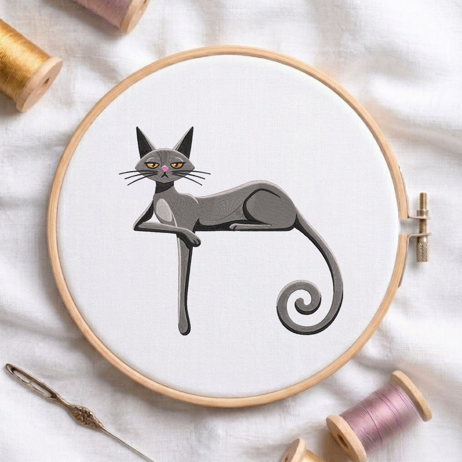 A white fabric stretched in a wooden embroidery hoop, featuring an embroidered grey cat with yellow eyes, a pink nose, long legs resting on its arm, and a curly tail.