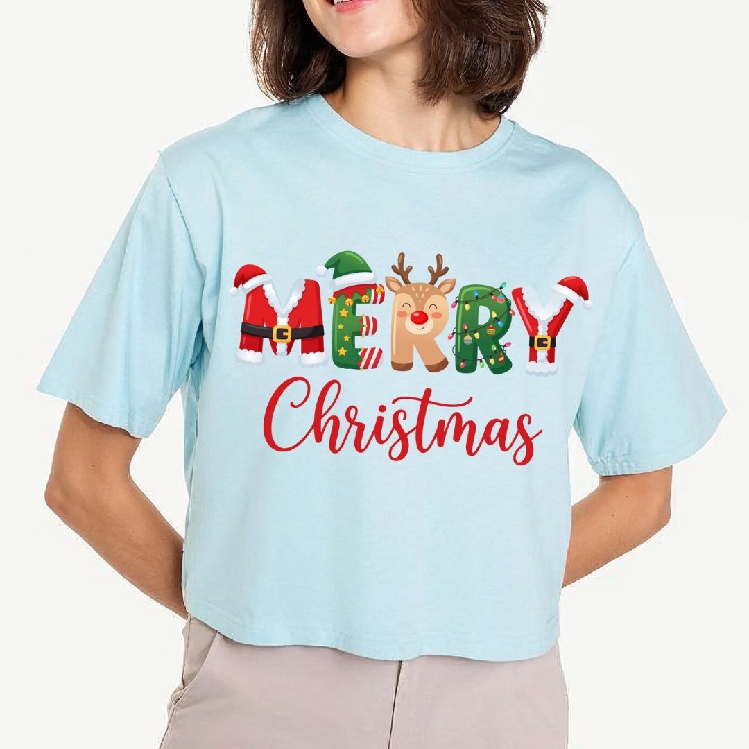 Woman wearing a light blue cropped t-shirt featuring a "MERRY Christmas" sublimation design with Santa, elf, reindeer, and string lights graphics.