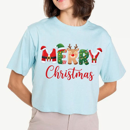 Woman wearing a light blue cropped t-shirt featuring a "MERRY Christmas" sublimation design with Santa, elf, reindeer, and string lights graphics.