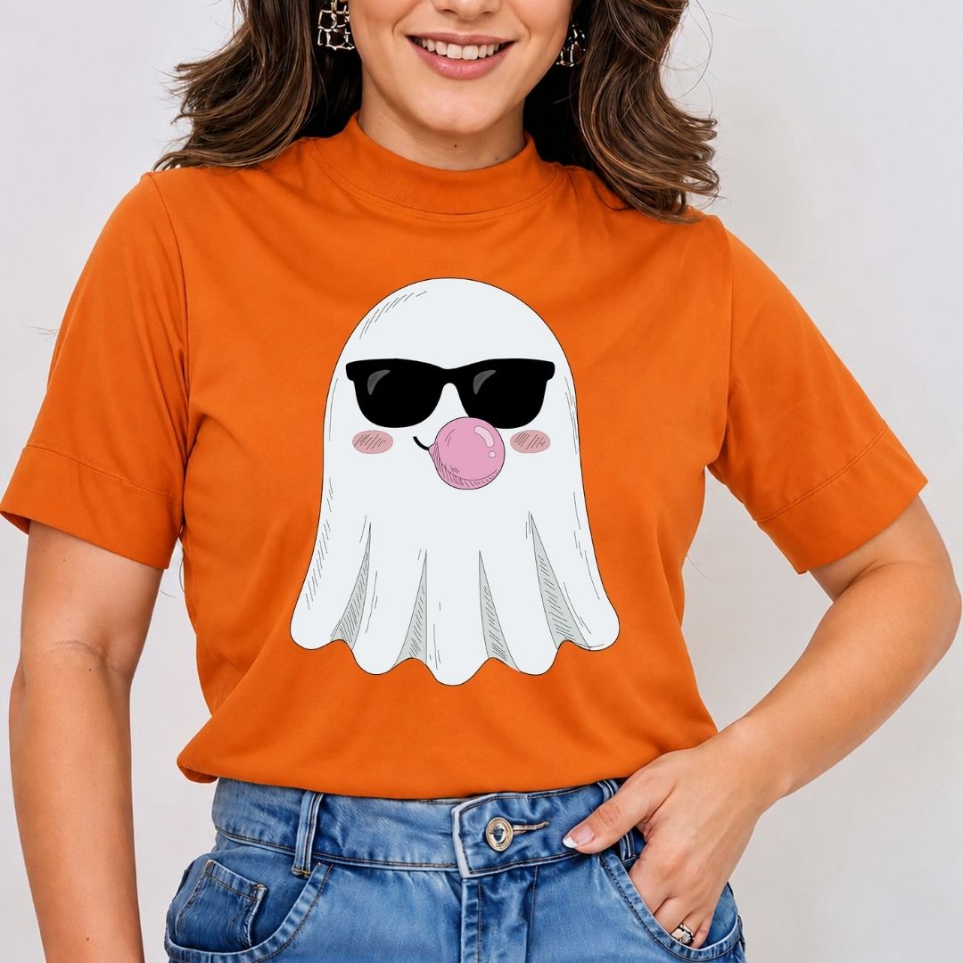 A woman wearing a bright orange short-sleeve t-shirt with a cartoon ghost graphic wearing black sunglasses and blowing a pink bubblegum bubble. She is also wearing blue jeans against a plain light gray background.