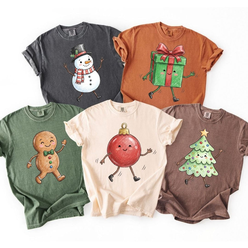 Five short-sleeve crewneck t-shirts in different colors, each featuring a different cute cartoon holiday graphic, arranged in a flat-lay style on a white background.