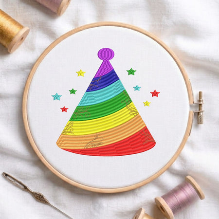 A circular embroidery hoop on white fabric holds a colorful stitched party hat design with rainbow stripes and small stars. Spools of thread and a needle are arranged around it as styling props.