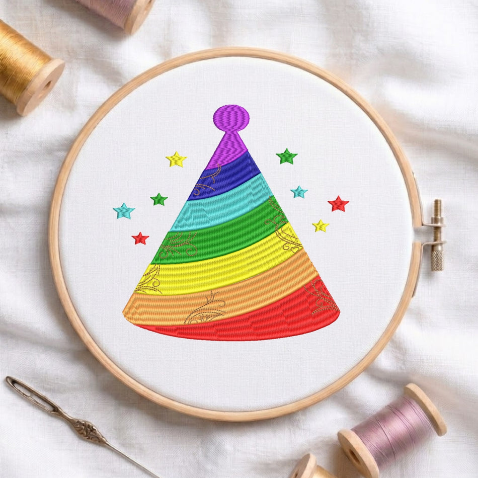 A circular embroidery hoop on white fabric holds a colorful stitched party hat design with rainbow stripes and small stars. Spools of thread and a needle are arranged around it as styling props.