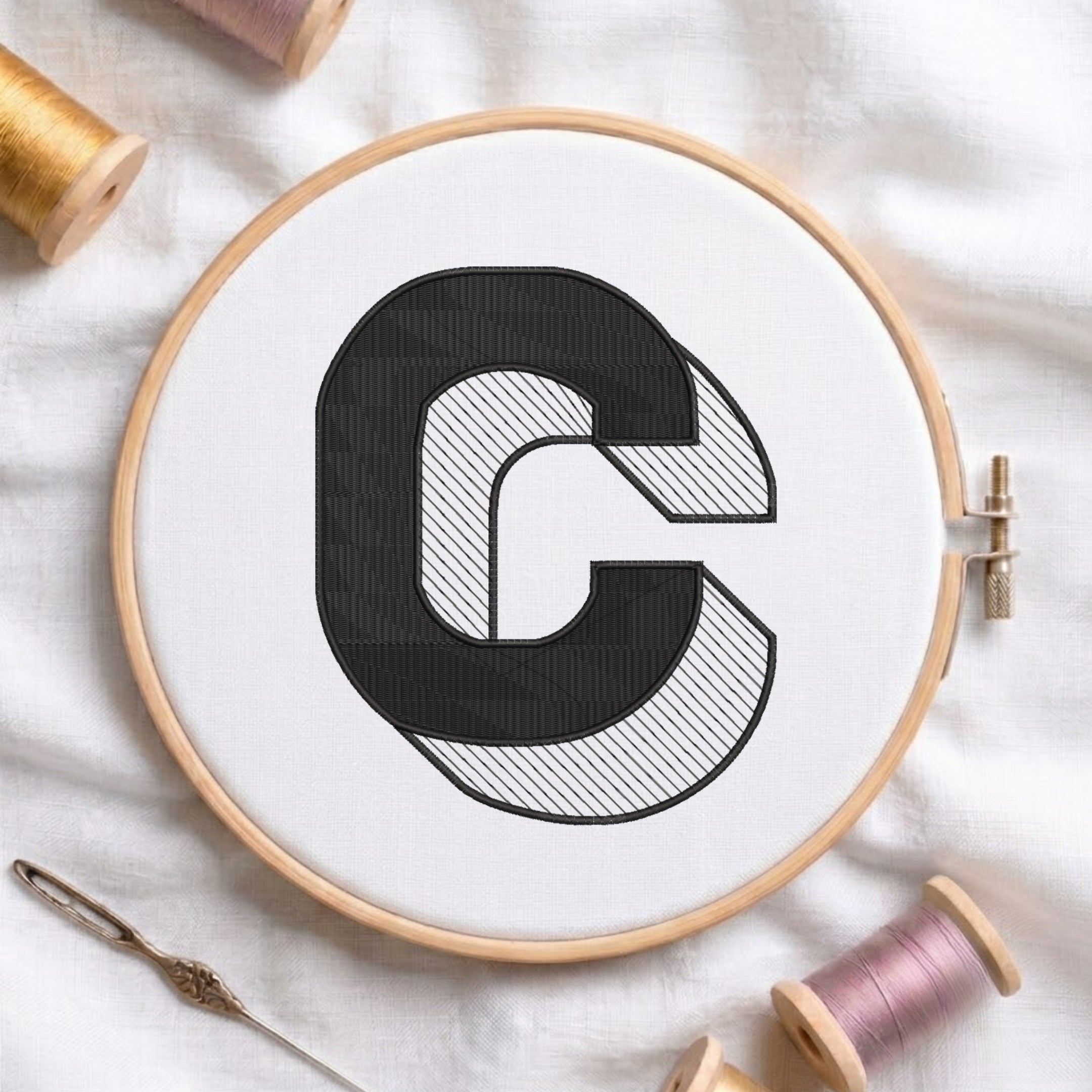 An embroidered 3D block uppercase letter "C" with striped shading texture, stitched inside a wooden hoop on white fabric with sewing threads.