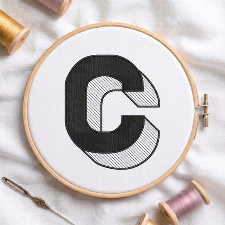 An embroidered 3D block uppercase letter "C" with striped shading texture, stitched inside a wooden hoop on white fabric with sewing threads.