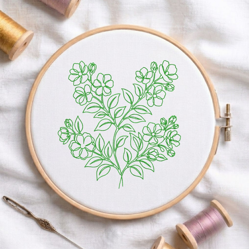 The green floral line-art design is displayed inside a wooden embroidery hoop, surrounded by thread spools and a needle on a white fabric background.