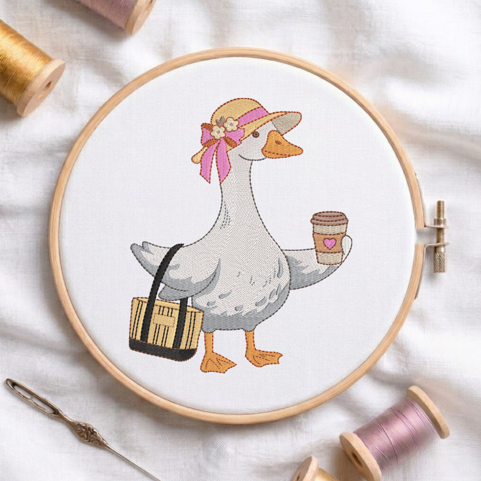 A cross-stitch embroidery design of a white goose wearing a tan hat with a pink bow and carrying a black-and-tan bag, shown inside a wooden embroidery hoop on a white fabric background with spools of thread and a needle nearby.