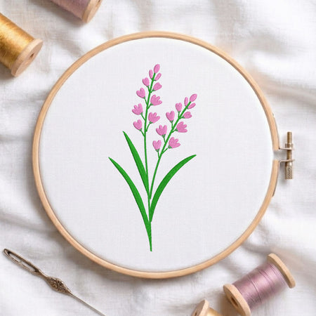 Pink lavender sprigs with green stems and leaves embroidered inside a round wooden hoop surrounded by thread spools.