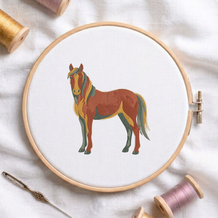 Vibrant stylized horse machine embroidery design displayed inside a round wooden hoop on white fabric alongside thread spools and a needle.