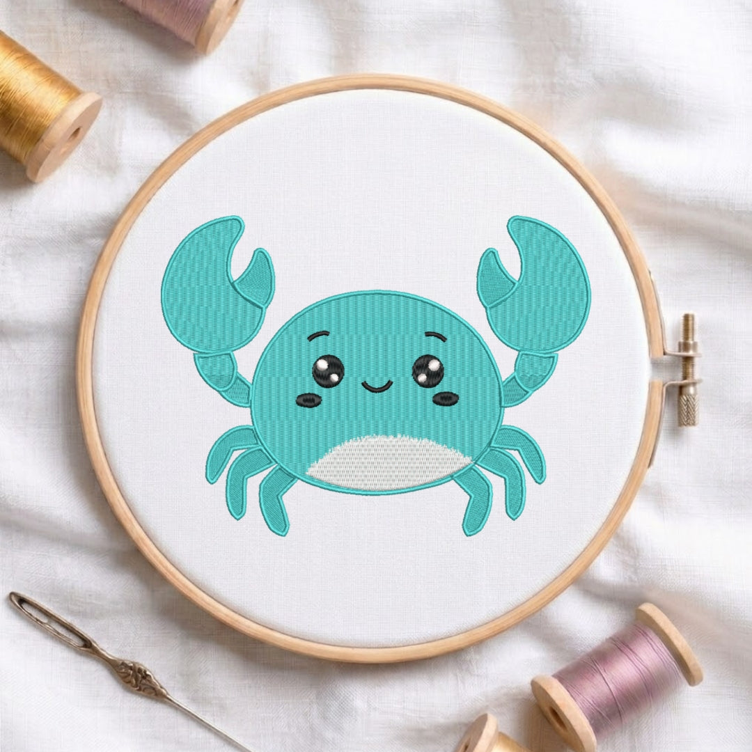A round embroidery hoop holding white fabric with a cute turquoise crab design stitched in the center. The hoop is styled on a white fabric background with spools of thread and a needle around it.