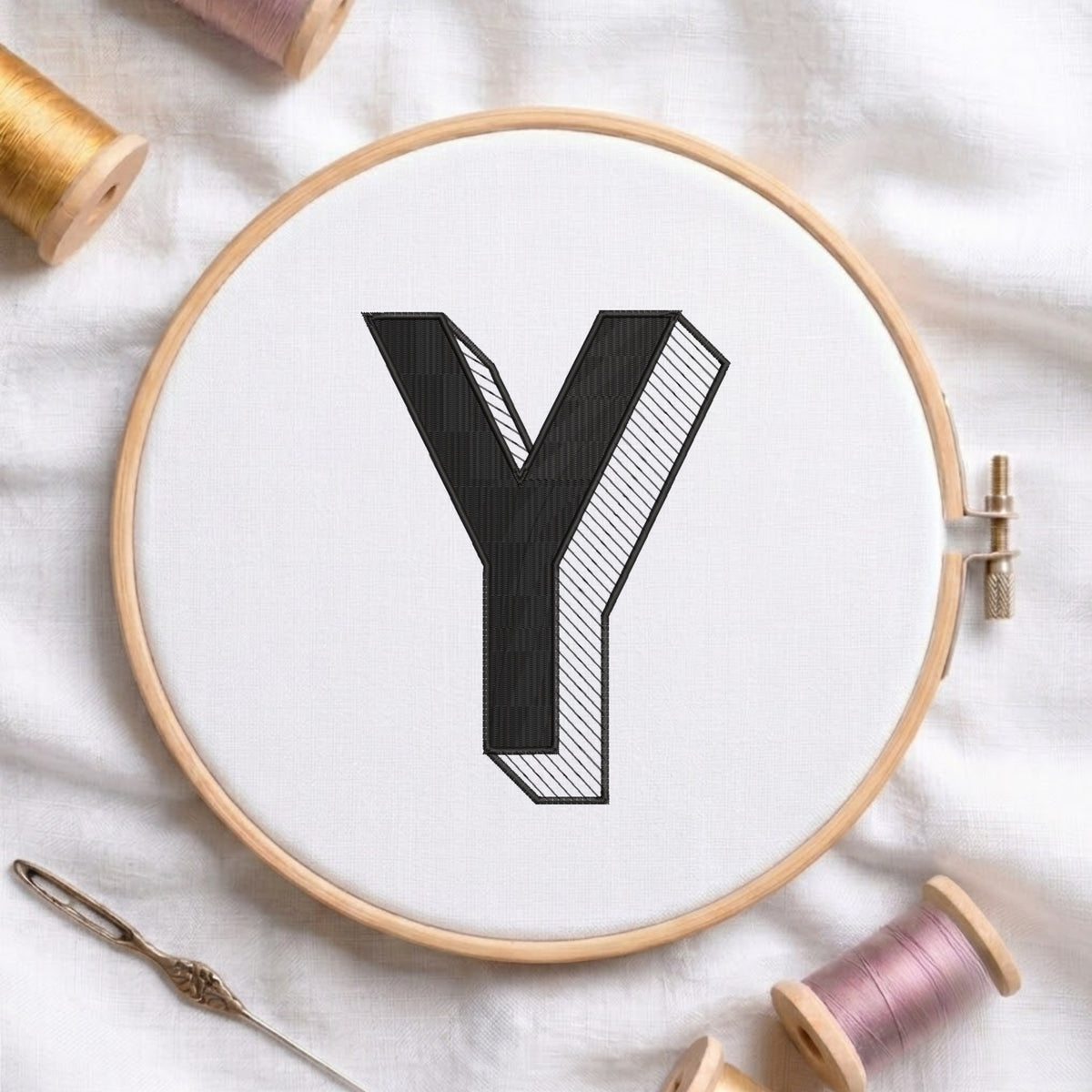 An embroidered 3D block letter "Y" with striped shading texture, stitched inside a wooden hoop on white fabric with sewing threads.